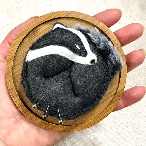 Sleeping badger pincushion. Curled up on side.Fixed to a bamboo pin dish. Held in the palm of a hand