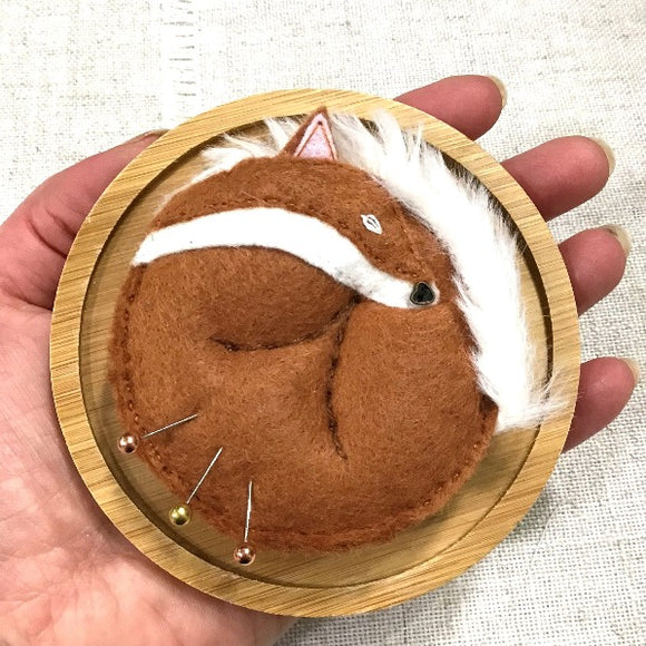Hand sewn felt fox pincushion. Red fox sleeping curled up on side, on a circular bamboo pin dish. Held in the palm of a hand.